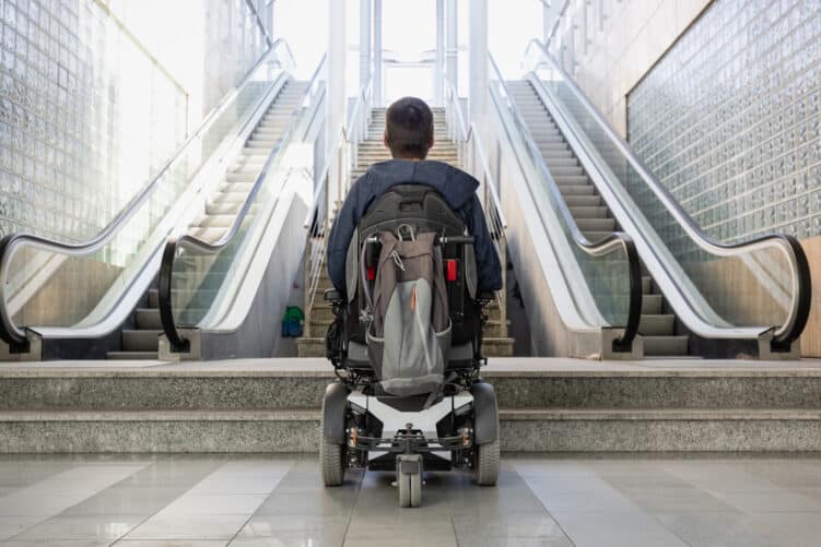 Mann mit Rollstuhl steht vor Treppen und Rolltreppen